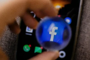 Hand holding magnifying glass over Facebook
